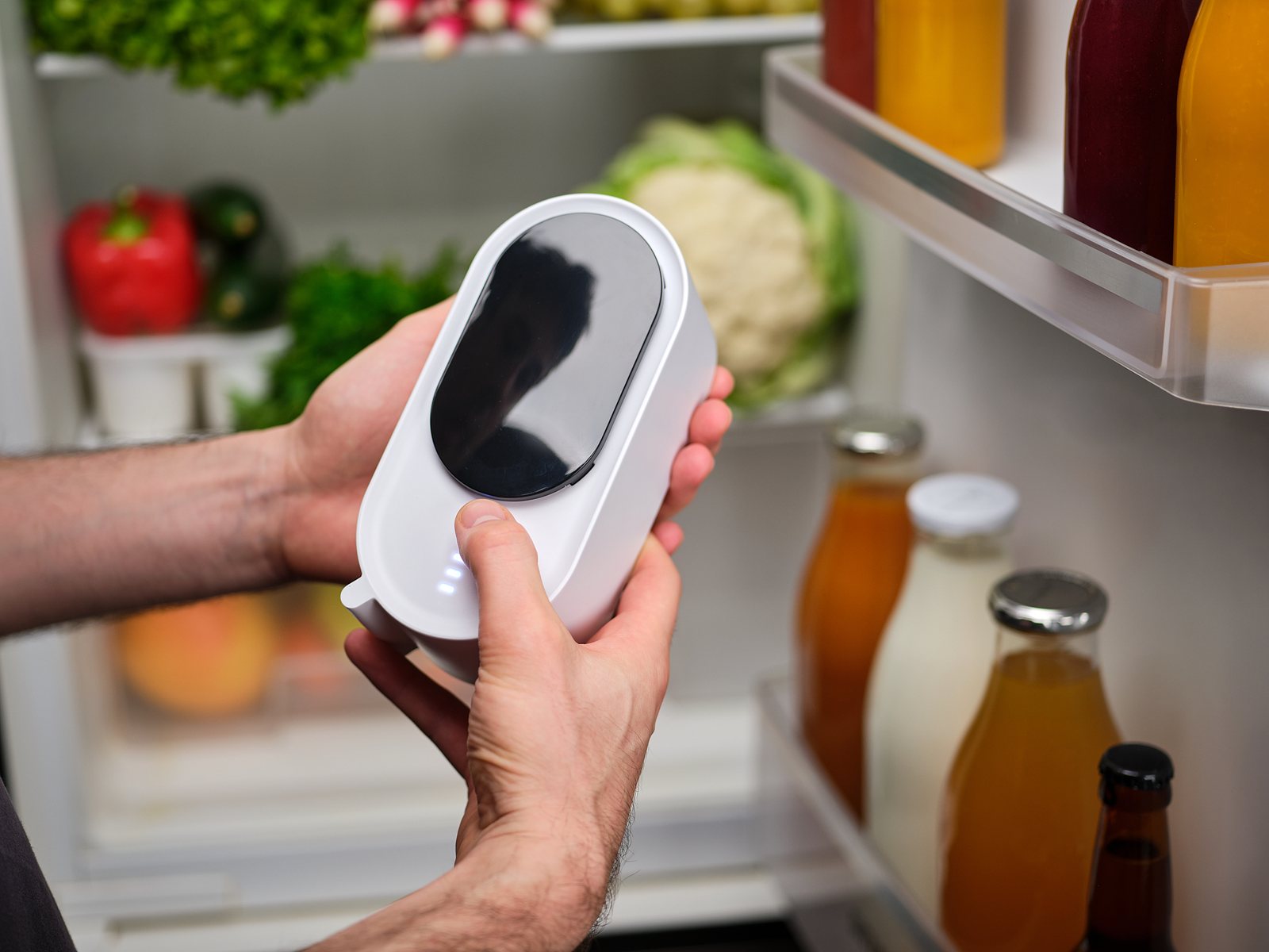 Une main active Holus devant un réfrigérateur ouvert rempli de fruits, légumes et boissons